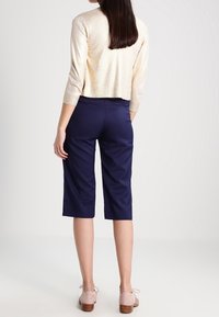 Lichtgouden cropped trui met driekwartmouwen gecombineerd met marineblauwe culottes. De outfit heeft een gladde textuur en een casual ontwerp.