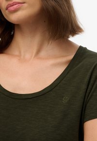 Olivenfarvet T-shirt med en rund udskæring, korte ærmer og subtil tekstur. Har et lille broderet logo på brystet.