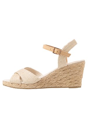 Beige vävd espadrille kilklack sandal med en texturerad tygöverdel, korsade remmar och en ankelrem som säkras med en guldtonad spänne.