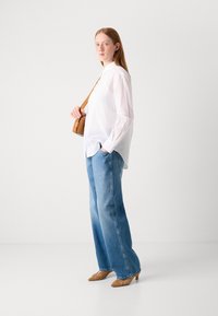 White button-up shirt with long sleeves, paired with light blue wide-leg jeans and brown textured heels. Brown crossbody bag worn.