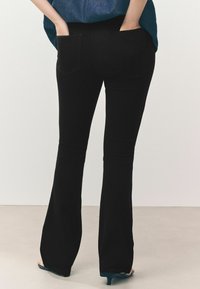 Zwarte flared jeans met een gladde textuur, voorzien van twee achterzakken en een high-waist ontwerp, gedragen met een casual, losse blauwe top.