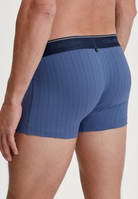 Blue ribbed boxer shorts with a snug fit, featuring a dark waistband labeled "CALIDA" and minimalistic stitching details.