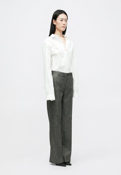 Bijela košulja dugih rukava s gumbima na izrezu, u kombinaciji s hlačama s visokim strukom u sivoj prugastoj boji. Crne cipele s oštrim vrhom upotpunjuju izgled.