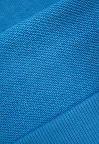 Niebieska próbka tkaniny o teksturowanym splocie. Posiada żebrowany brzeg. Jednolity kolor w całym materiale, bez widocznych wzorów czy dekoracji.