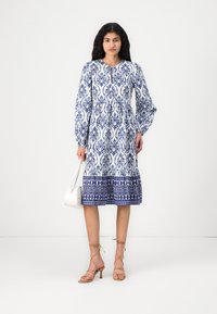 Rochie midi albă și albastră cu un model floral. Dispune de mâneci lungi tip puff, de un decolteu rotund și de un tiv cu o margine decorativă.