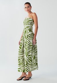 Grøn- og hvidstribet stropløs kjole med rynket krop og flagrende nederdel, lavet af letvægtsstof. Modellen har sorte klipklappere på.