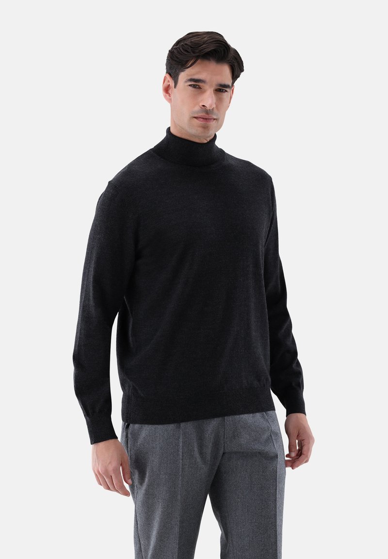 Schwarzer Rollkragenpullover aus einer weichen Wollmischung, mit lockerer Passform und geripptem Saum, kombiniert mit grauen Hosen.