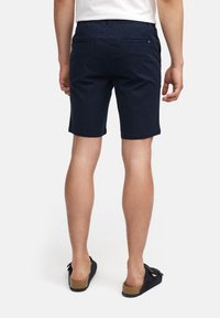 Shorts in cotone blu navy con una vestibilità rilassata, due tasche posteriori e una cintura elastica. Indossati con sandali neri.