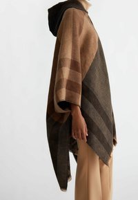 Hnědý pončo se vzorem a kapucí, obsahující kombinaci kostkovaného a diagonálního pruhování, vyrobené z texturované tkaniny. Okraje jsou třásňové.