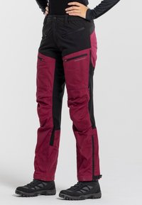 Outdoor pants featuring a mix of burgundy and black fabric, reinforced knees, multiple zippered pockets, and adjustable cuffs.