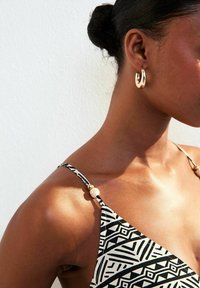 Maillot de bain à motifs noir et blanc avec de fines bretelles ornées de perles dorées et crème, mettant en valeur un décolleté élégant.
