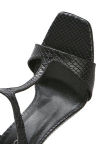 Sandal nero con un motivo a pelle di serpente testurizzato, punta quadrata e lati aperti. Il materiale è liscio con una finitura lucida.