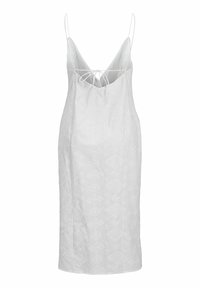Vestido blanco sin mangas con un escote en V profundo, cierre ajustable con lazo en la parte posterior, tejido texturizado con sutiles patrones en toda su superficie.