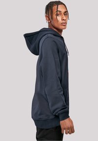 Navyblauer Hoodie aus weichem Material, mit einer Fronttasche und verstellbarem Kordelzug. Mit buntem Logo auf der Brust und gerippten Bündchen.