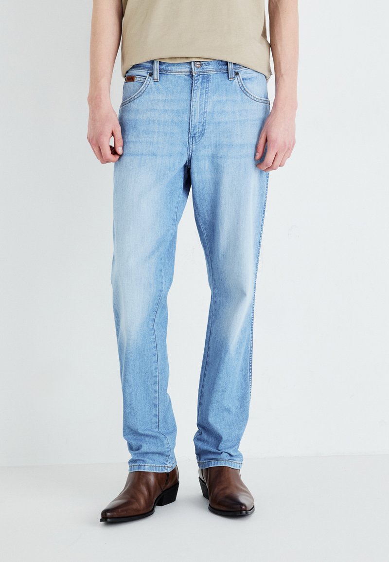Jeans din denim albastru deschis, cu o croială relaxată, având un design clasic cu cinci buzunare și zone decolorate. Asortați cu bocanci din piele maro.