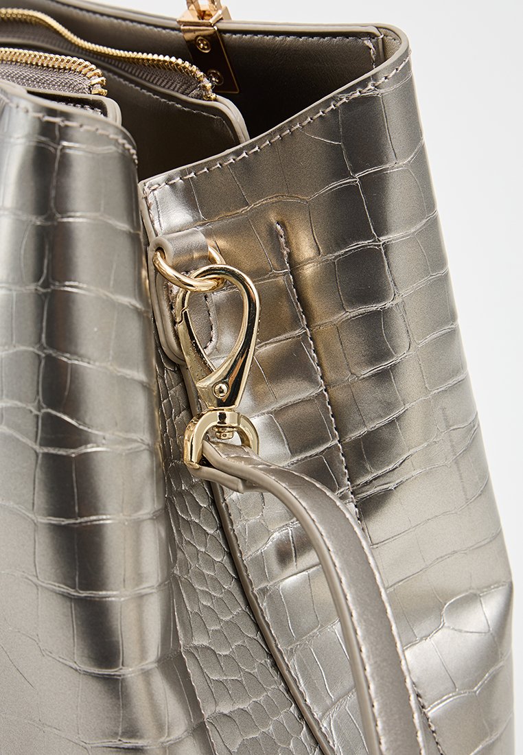 Sac à main argenté métallisé avec une texture crocodile, comportant un fermoir en métal doré et une bandoulière lisse. Intérieur visible avec un détail de fermeture éclair.
