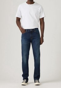 Mörkblå jeans i denim med rak skärning, kombinerade med en enkel vit t-shirt och svarta sneakers. Minimal sömnad och inga synliga mönster.