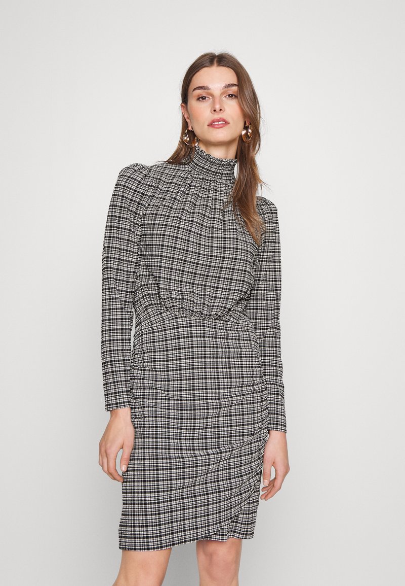 Rochie în carouri alb-negru, cu guler înalt, mâneci lungi și un design strâns la talie, având o textură netedă și o croială ajustată.