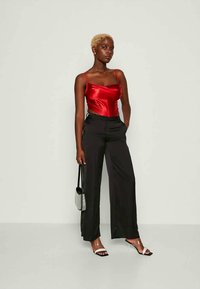 Red satin camisole with thin straps, paired with black wide-leg trousers. Model holds a small silver bag and wears clear heeled sandals.
