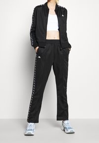 Svart träningsoverall med jacka med dragkedja och byxor med elastisk midja, med en mjuk textur, vita logotypdetaljer och kontrasterande sidostripes.