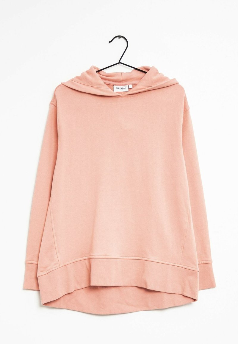 Sweat-shirt à capuche rose doux avec manches longues, détails de couture avant et une ourlet arrière légèrement plus long, suspendu à un cintre noir.