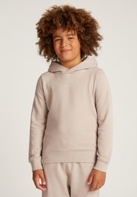 Bambino con i capelli ricci che indossa un hoodie beige di Calvin Klein e pantaloni abbinati, in piedi contro uno sfondo chiaro e neutro.