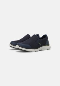 Tengerészi slip-on cipők texturált hálós felsőrésszel, kontrasztos gumitalppal és diszkrét sárga logóval. Rugalmas kialakítás a kényelem érdekében.