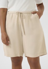 Beige shorts made of lightweight fabric, featuring an elastic waistband, drawstring closure, and side pockets with a relaxed fit.
