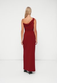 Rochie maxi burgundy cu un decolteu drapat, croi slim și detalii aurii la umeri. Țesătură fină cu un ușor luciu.