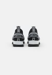 Pár černobílých slip-on tenisek DKNY zobrazených zezadu s elastickými páskami s logem a masivními bílými podrážkami na bílém pozadí.