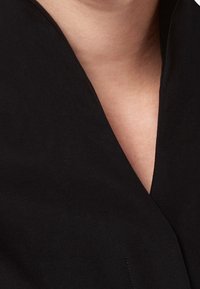 Sort stof med en glat tekstur har en V-formet halsudskæring og et simpelt design, der understreger minimalisme uden yderligere detaljer.