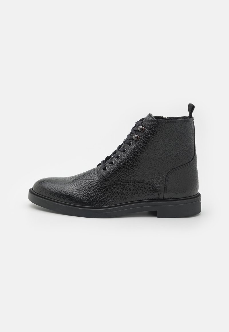 Botas de tobillo de cuero negro con un acabado texturizado, punta redonda, diseño con cordones y una suela de goma baja. Incluye una pestaña en la parte posterior.
