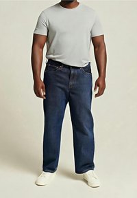 T-shirt gris à manches courtes associé à un jean en denim bleu foncé, avec une coupe droite et des coutures apparentes sur les poches.