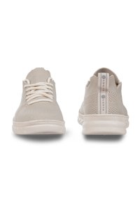 Beige knit sneakers with round toe, flat laces, and textured fabric. Accented with a pull tab at the heel and smooth rubber sole.