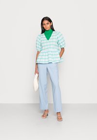 Calças azul claro combinadas com um top verde de gola alta e uma blusa peplum aos riscas, com mangas bufantes, em verde menta e branco. Tecido texturizado.