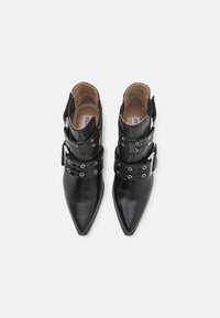 Botas de tobillo de cuero negro con punta afilada, lados cortados y múltiples hebillas. Presentan detalles de ojales metálicos y una textura suave.
