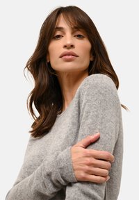 Szary sweter dziewiarski z okrągłym dekoltem i długimi rękawami. Miękka tekstura z prążkowanymi mankietami. Naturalne światło podkreśla detale tkaniny.