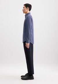 Camicia a maniche lunghe blu navy con un motivo a pois, abbinata a pantaloni e scarpe neri, vista di lato.