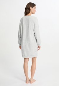 Abito grigio chiaro a maniche lunghe, di lunghezza al ginocchio, realizzato in tessuto morbido. Presenta una vestibilità ampia e un orlo arrotondato con una sottile texture.