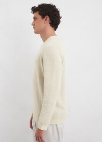 Light beige long-sleeve sweater in soft knit fabric, featuring a crew neck and ribbed cuffs, shown from the side against a plain background.