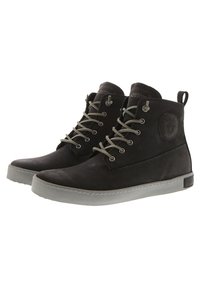 Botas de cuero negras de media caña, con cordones grises, un parche con logo redondo y una suela de goma gris. Textura suave, diseño sencillo.