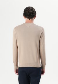 Beige kötött pulóver hosszú ujjakkal, V-alakú hátsó nyakkivágással és bordázott mandzsettákkal. Texturált anyag, egyszerű és minimalista dizájn.