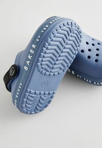 Modré gumové sabotky s perforovaným vrchom, čiernym nastaviteľným popruhom, textúrovanou podrážkou a bielym písmenom s nápismi „TED BAKER“ a „BAKER“. 
