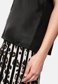 Schwarzes Oberteil mit einer glatten Textur, ausgestattet mit einem glänzenden Knopf am Saum. Kombiniert mit einem gestreiften Rock in Beige und Schwarz, verziert mit einem Leopardenmuster.