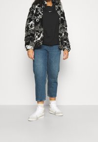 Mönstrad pl plush-jacka i svart och vitt, svart sweatshirt med logo, blå beskurna jeans och vita högklackade sneakers med dubbla remmar.