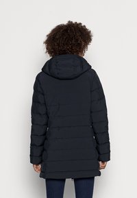 Tumma tyynyvuorattu takki, jossa on huppu; siinä on vaakasuora tikkaus, pitkät hihat ja puolipitkä leikkaus, valmistettu sileästä materiaalista.