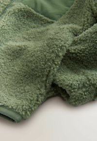 Olivovo zelená fleece textília s mäkkým, textúrovaným povrchom. Má hladký okraj a nadýchaný, pohodlný vzhľad. Vhodná na vonkajšie oblečenie.