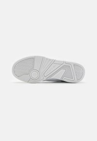 Fehér gumitalpú sneaker, mintázott talprésszel, barázdákkal és kör alakú emblémával, az oldalán "LACOSTE" felirattal.