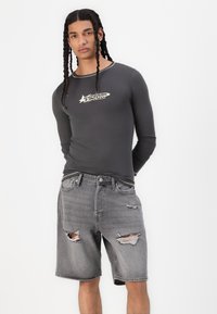T-shirt à manches longues gris avec un logo graphique sur la poitrine, associé à un short en denim gris usé avec des bords effilochés et des poches.