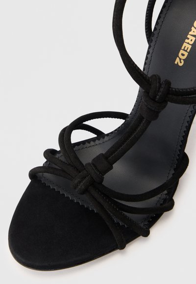 Sandal in suede nero con tacco alto, design a fasce incrociate, punta affusolata e fodera interna testurizzata. Presenta dettagli annodati.